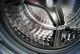 Inside view of a shiny stainless steel washing machine drum with perforated walls.