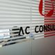 Ufficio con vetro striato e scritta "AC CONSULTING", persona al computer sullo sfondo.