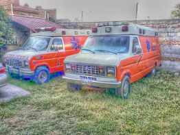 Dos ambulancias antiguas naranjas estacionadas en un patio con hierba.