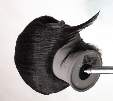 Testa di manichino con capelli scuri lisci su supporto metallico, vista laterale.