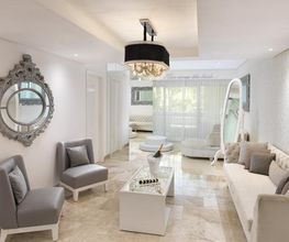 Sala moderna con sillones grises, mesa blanca, espejo decorativo y lámpara colgante.