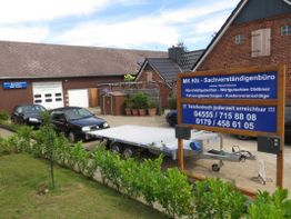 Zwei schwarze Autos und ein Anhänger stehen vor einer Garage. Blauer Schild des Kfz-Büros.