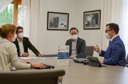 Quattro persone sedute con mascherine in una riunione attorno a un tavolo in ufficio.