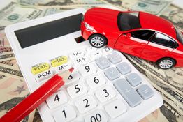 Calculator, red toy car, and pencil on scattered dollar bills.