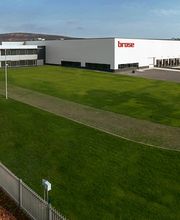 Edificio industrial blanco con logo "brose", rodeado de césped verde y cielo azul.