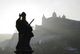 Silhouette einer Statue vor einer dimmen Festung auf einem hügeligen Gelände im Nebel.
