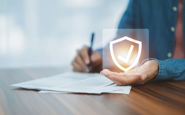 Hand hält ein animiertes Schutzschild in der linken Hand, während er mit der rechten Hand einen Vertrag überfliegt.