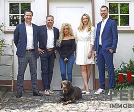 Fünf Personen und ein Hund vor einem Gebäude mit dem Schild "Fels Immobilien".