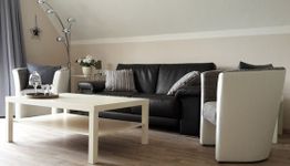 Modernes Wohnzimmer mit schwarzem Sofa, Couchtisch und Sesseln unter Dachschräge.