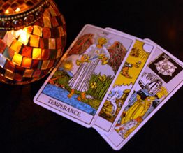 Cartas del tarot junto a una vela decorativa encendida sobre fondo oscuro.