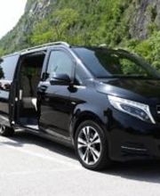 Eine Person im Anzug steht neben einem schwarzen Mercedes-Van im Freien.