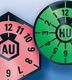 Rosa und grüne Prüfplaketten für Abgasuntersuchung (AU) und Hauptuntersuchung (HU).