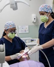 Dos dentistas con mascarillas atienden a un paciente en un consultorio dental.