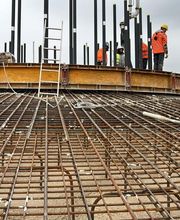 Bauarbeiter in orange Kleidung arbeiten auf einer Baustelle mit Stahlverstrebungen und Leitern.