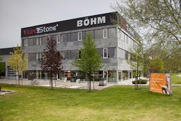 Ein modernes Bürogebäude mit "BÖHM" und "Vider Stone" Beschriftung, umgeben von Bäumen.