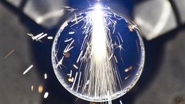 Scintille luminose esplodono all'interno di una bolla trasparente su sfondo scuro.