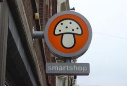 Rond bord met paddenstoel en tekst "smartshop" aan een gevel.