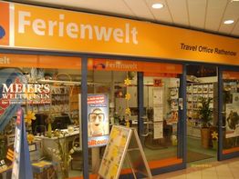 Reisebüro "Ferienwelt" mit gelbem Schild, Schaufenster voll mit bunten Plakaten und Broschüren.