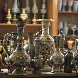 Ornate metal vases displayed on wooden shelves in a well-lit shop setting.