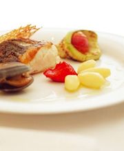 Plato gourmet con pescado, almejas, papas y verduras en un plato blanco, tenedor a un lado.