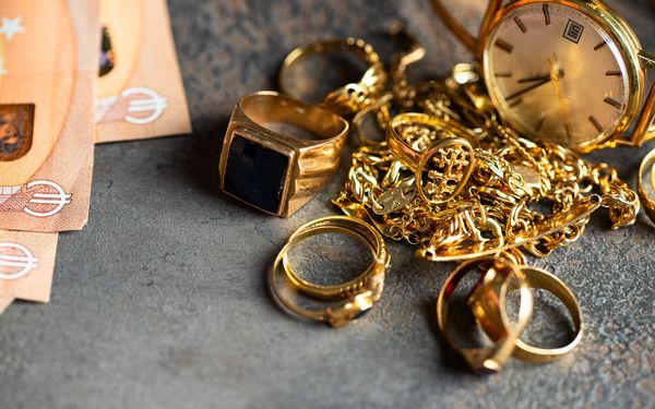 Goldschmuck liegt auf dem Tresen eines Juweliers, neben aufgefächertem Bargeld.