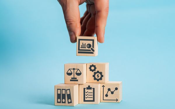 Holzwürfel mit Symbolen für Recht, Finanzen, Dokumente und Unternehmensentwicklung als Darstellung verschiedener Unternehmensformen.