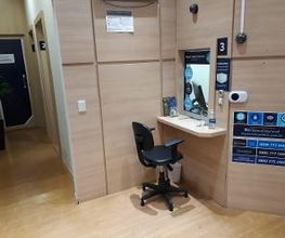 Corredor com mesa e cadeira de escritório em canto iluminado, perto de porta azul com números.
