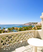 Balcón con vista al mar y palmeras bajo un cielo despejado y azul.