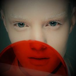 Frau mit blonden Augenbrauen hinter rotem Lichtfilter, grüner Blick, nahe Aufnahme.