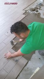 Uomo in posa pavimento in legno con martello di gomma, indossa maglietta verde.