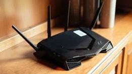 Black wireless router with four antennas on a wooden surface.