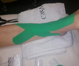 Pierna con cinta kinesiotape verde sobre una camilla blanca.