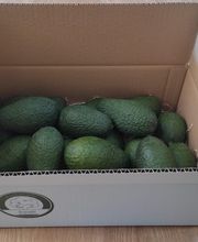 Caja de cartón abierta con varios aguacates en su interior sobre un suelo de madera.