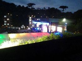 Show noturno ao ar livre com palco iluminado e pessoas ao redor em um parque.