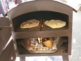 Zwei Flammkuchen im Holzofen backen, mit loderndem Feuer darunter.