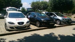 Tres coches aparcados en fila bajo árboles en un estacionamiento.