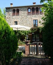 Casa de piedra rodeada de árboles y jardín, con sombrilla blanca en el patio.