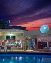 Edificio moderno frente a piscina al atardecer con cielo púrpura y palmera iluminada.