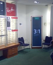 Opticienwinkel met brillen op displays en stoelen in een verlichte ruimte.