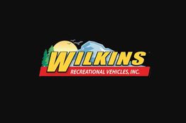 Wilkins Recreational Vehicles logo with a sun, mountains, and trees on a black background.