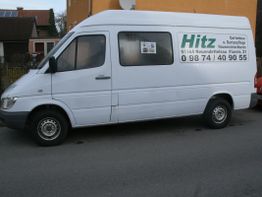 Weißer Lieferwagen mit Schriftzug "Hitz" und Kontaktdaten auf der Straße geparkt.
