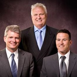 Three men in suits smiling against a dark background.