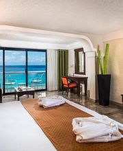 Habitación de hotel luminosa con vistas al mar, cama grande y televisor en la pared.