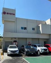 Edificio blanco con logo "Evonik" y cinco autos estacionados al frente en un día soleado.