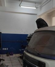 Oficina mecânica com van branca e azul, capô aberto, em ambiente iluminado.