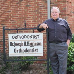 Man standing beside orthodontist sign with a brick wall background.