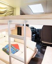 Interior de una autocaravana con cama, escaleras y manta de colores sobre el sofá.