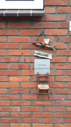 Welkom bord met kerstelf en miniatuurstoel tegen bakstenen muur.