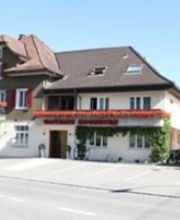 Zweistöckiges Haus mit rotem Schild und Terrasse, Fahrräder davor geparkt, sonniger Tag.