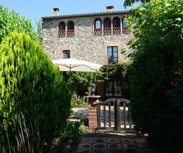 Casa de piedra rodeada de árboles y jardín, con sombrilla blanca en el patio.